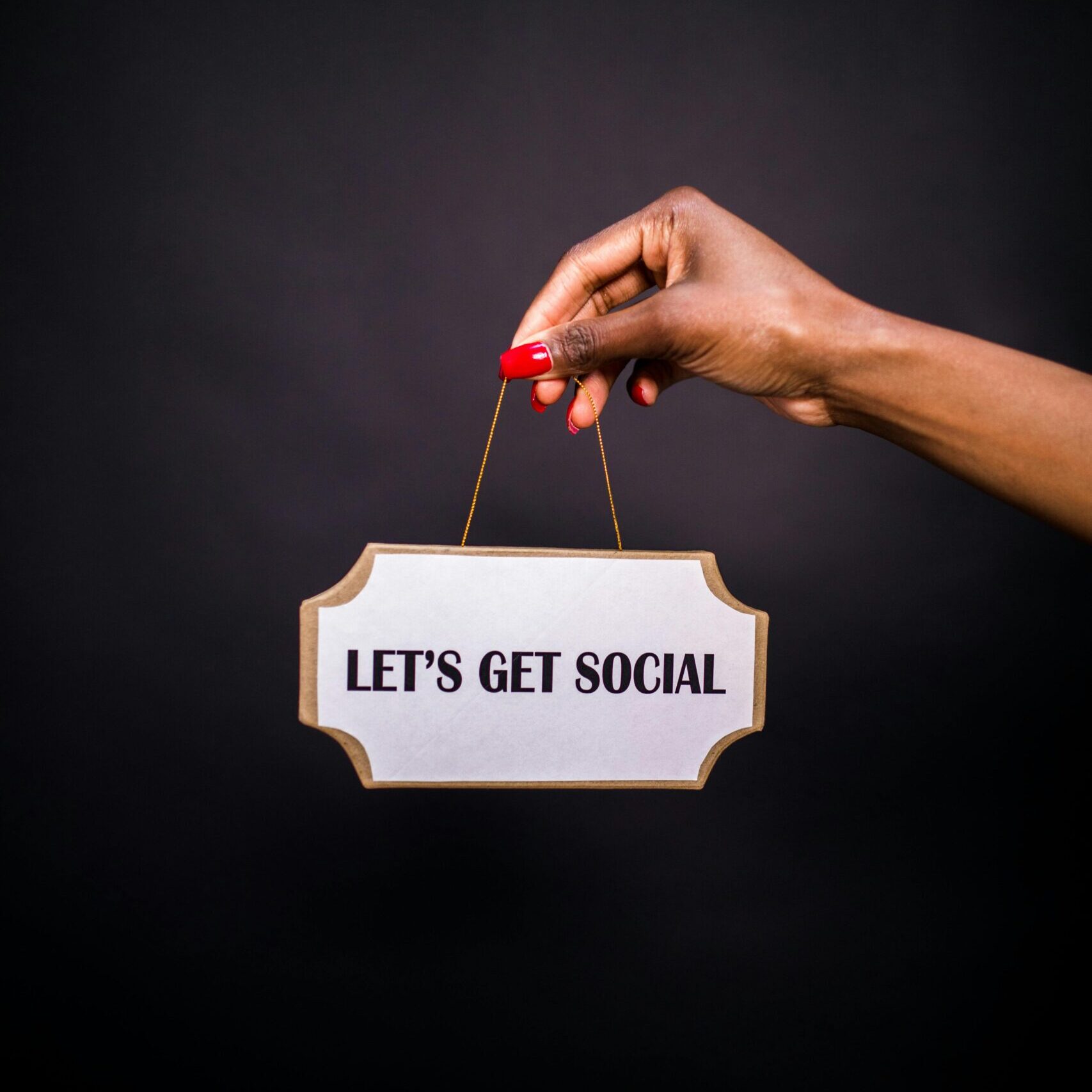 Close-up of a hand holding a sign with 'Let's Get Social' on a dark background.