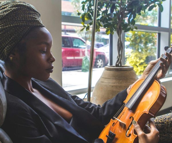 Elegant woman with turban practicing violin in cozy indoor setting.